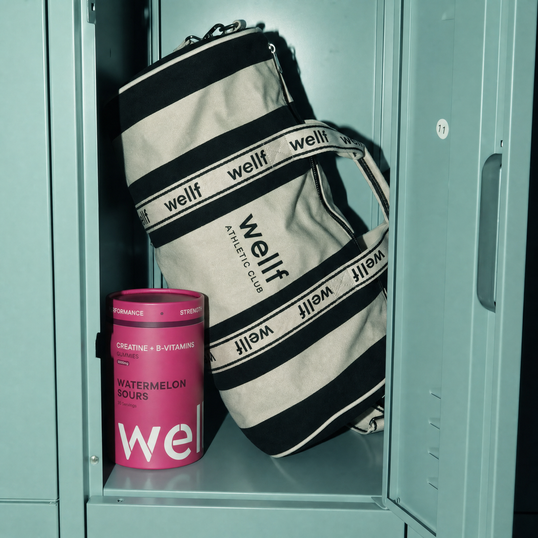 Tub of WELLF Watermelon Sours creatine sweets beside a striped WELLF Athletic Club kit bag in a teal gym locker